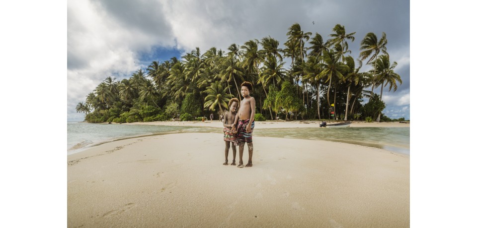 two children stand on sand on an island in the Pacific