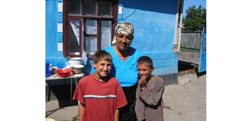 Woman and two young boys stand outside of house