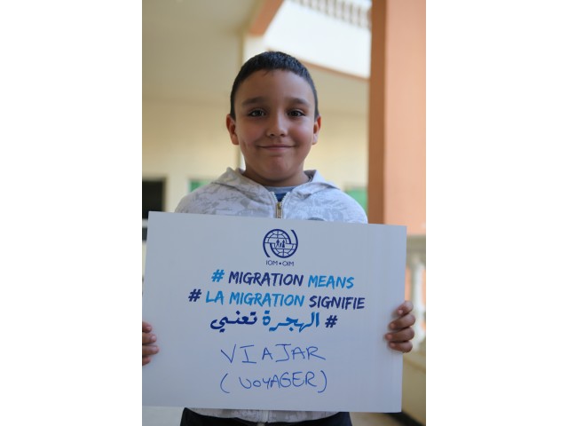 Image of a boy in Morocco holding up a sign saying migration means voyager