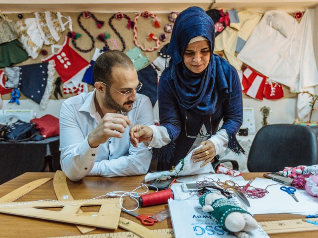 An image of a woman assisting a man with in a sewing class for men