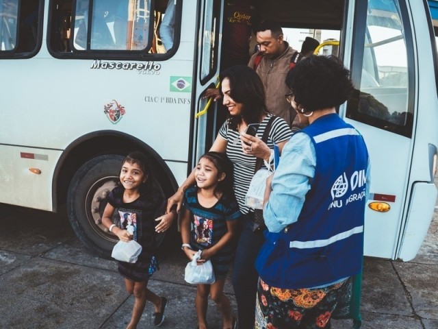 Children and their families arrive on a bus looking excited in IOM Brazil