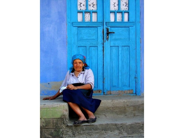 Elderly woman sits in front of a blue door to a home