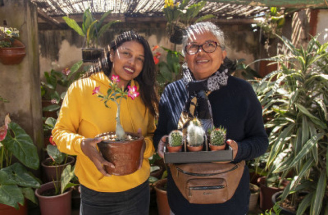 A young woman and and an old woman smiling to the camera with their hands holding some plants