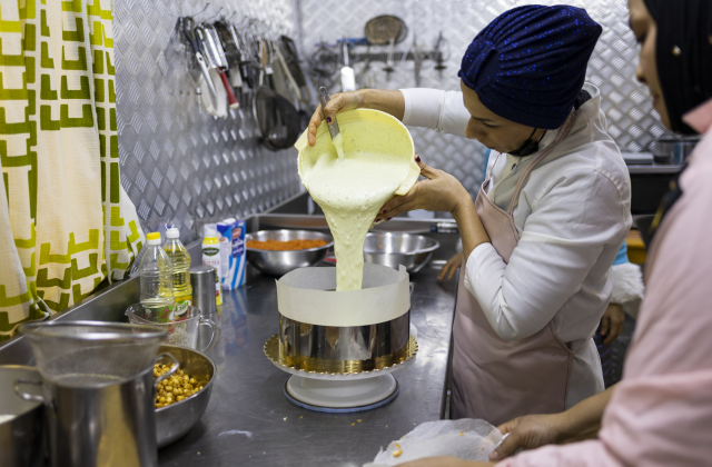 A woman baker pours cake batter into a tin at her business