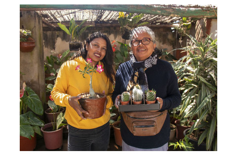 A young woman and and an old woman smiling to the camera with their hands holding some plants