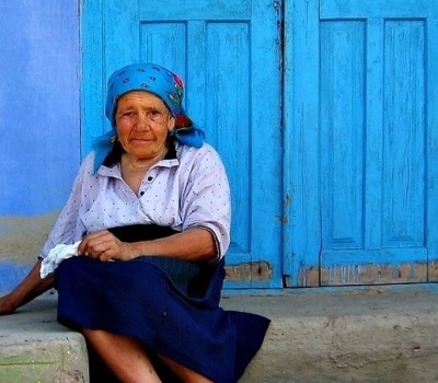Elderly woman sits in front of a blue door to a home