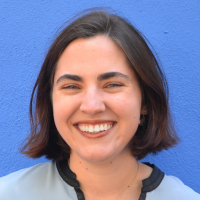 An image of Elizabeth, smiling while standing in front of a blue wall. 